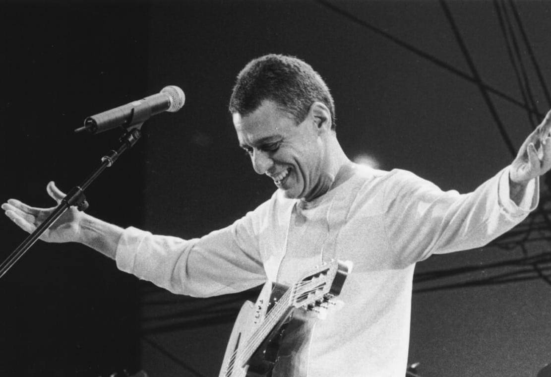 Chico Buarque tocando guitarra em apresenta\u00e7\u00e3o musical, imagem da exposi\u00e7\u00e3o fotogr\u00e1fica Imagens Musicais