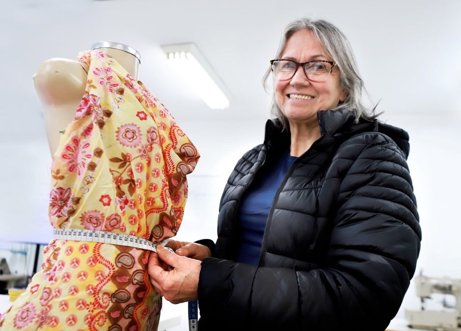 Aluna sorridente com fita métrica junto a manequim